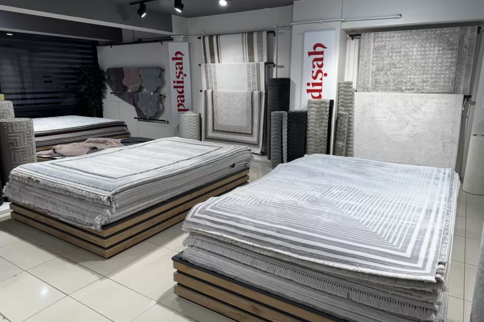 Mamak Çarşı İçi mağazamızın halı bölümünde üst üste serili ve askıda duran gri tonlu halılar